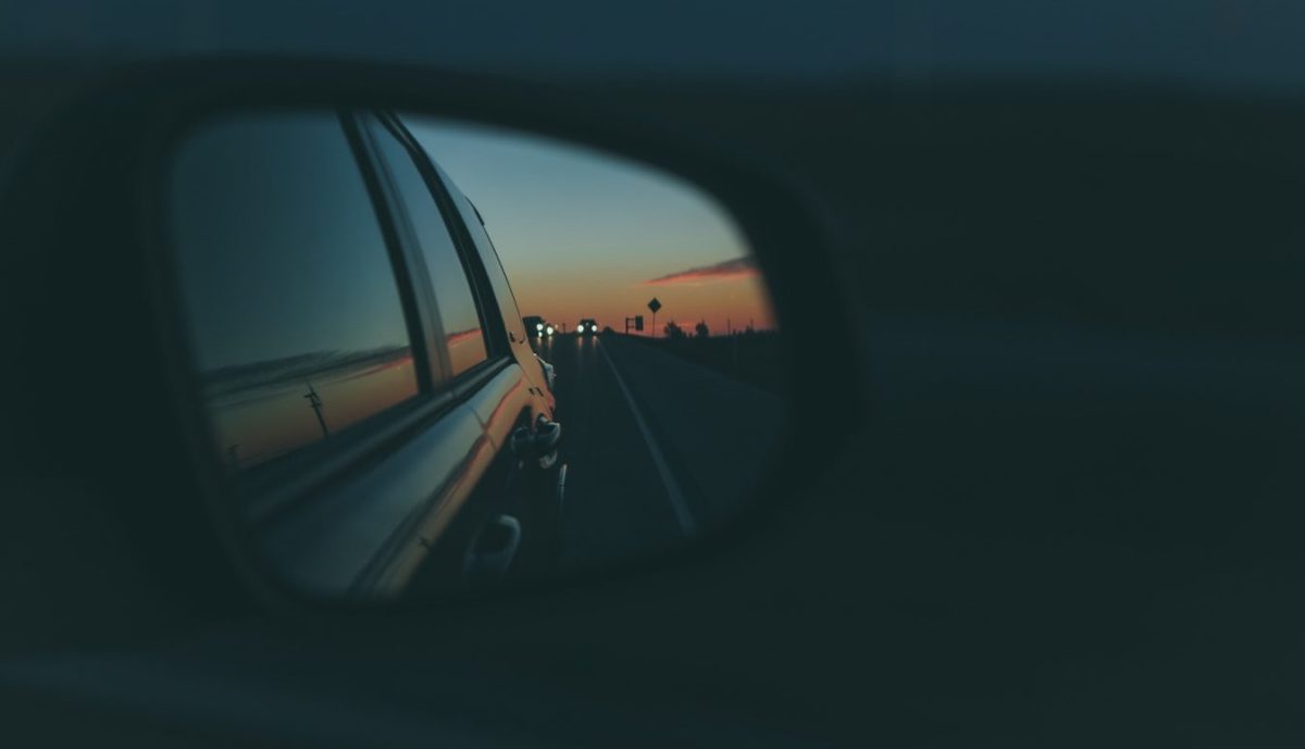 A car’s side view mirror shows a sunset.
