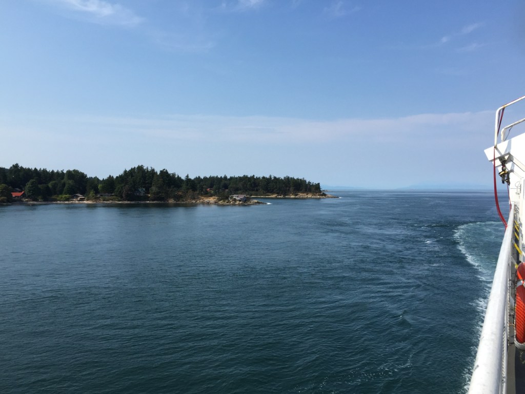 View of a tree-lined coast from the deck of a ferry sailing through the Strait of Georgia.